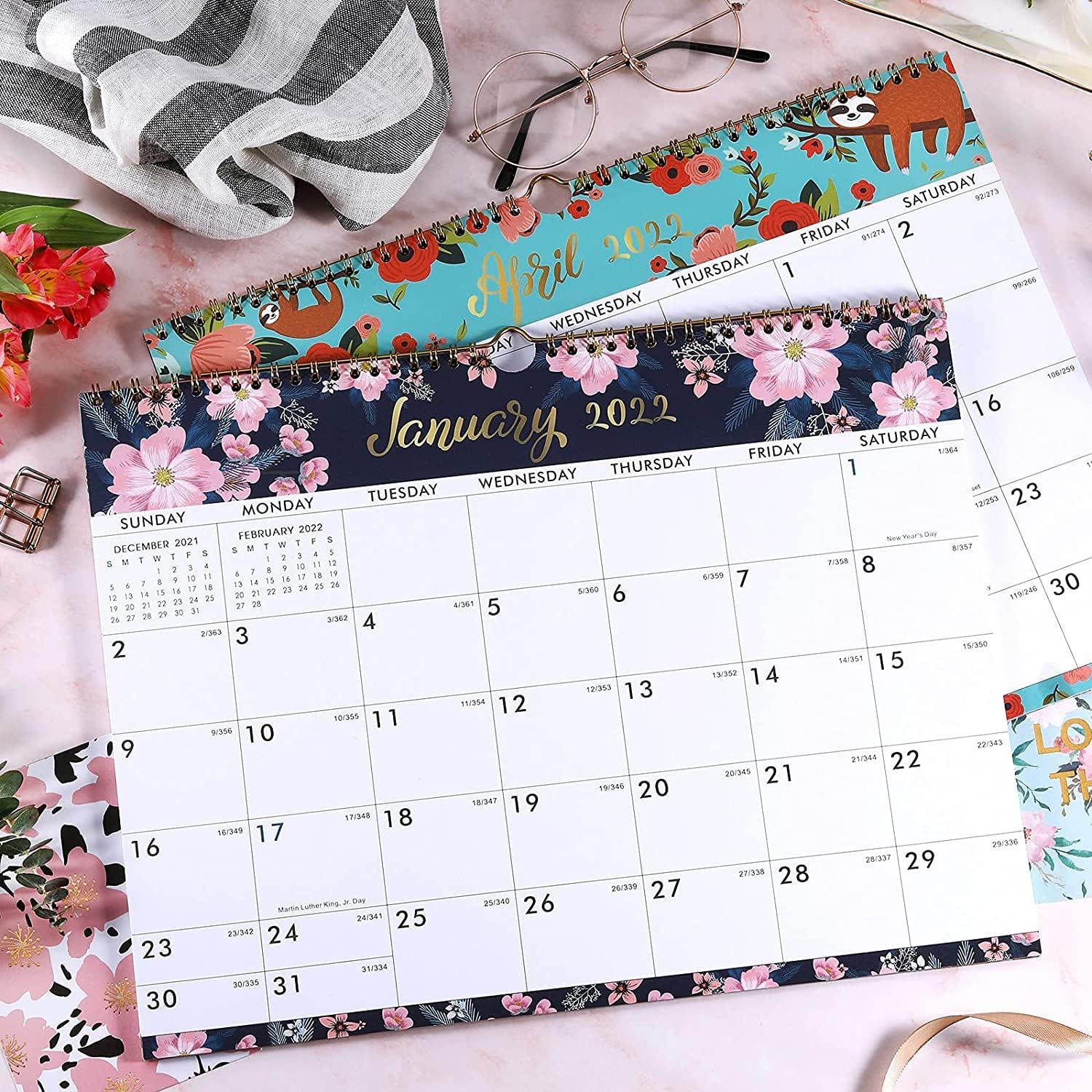 Floral wall calendars with gold-colored wire binding arranged on a pink desk